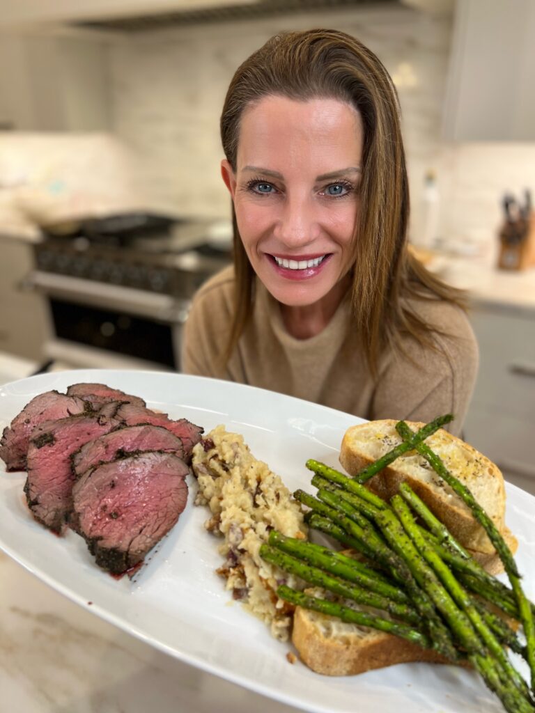 Tiffany Blackmon holding plated beef tenderloin with garlic mashed potatoes and roasted asparagus.