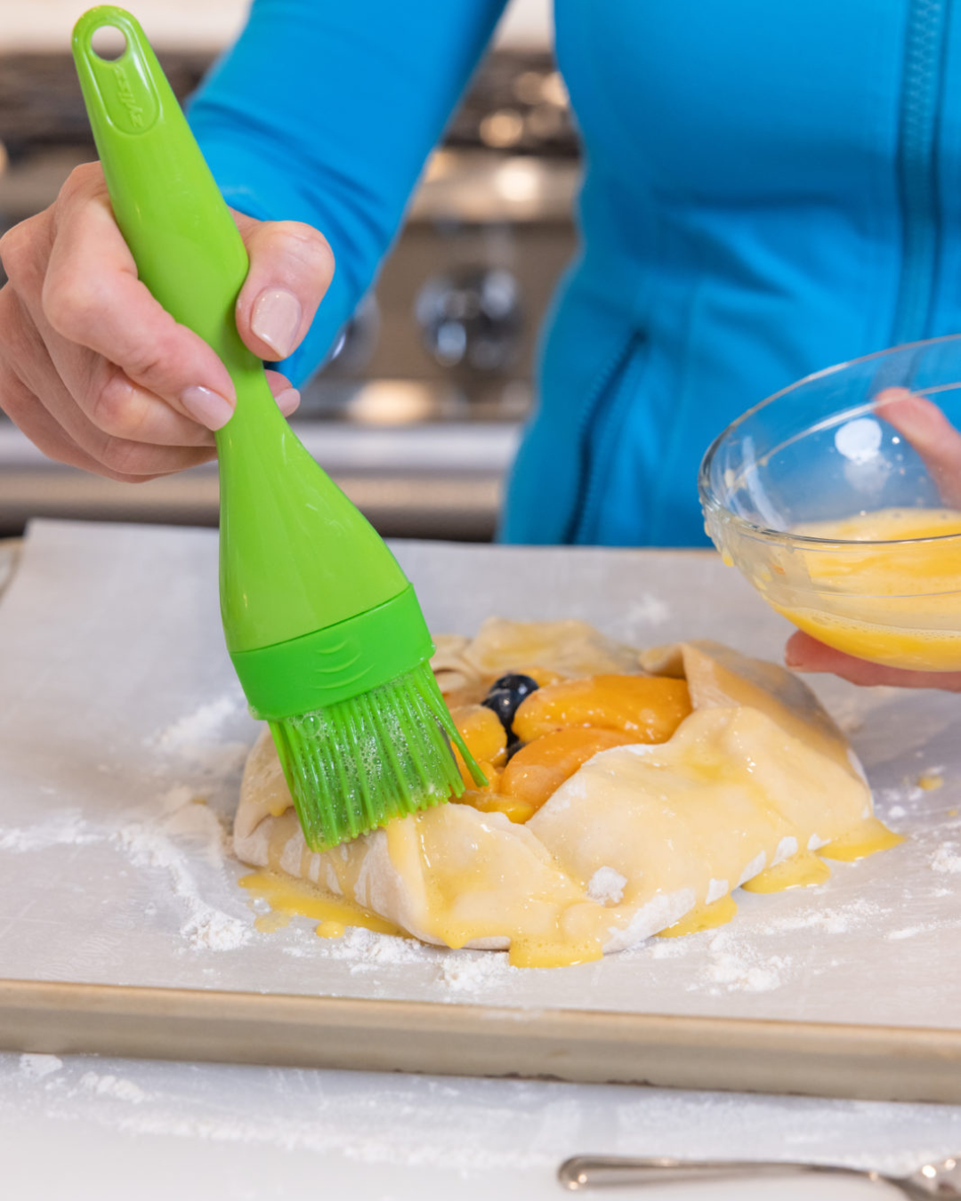 tiffany spreading melted butter on the pastry batter with the peach and blueberry filling inside, the perfect dessert for peach season