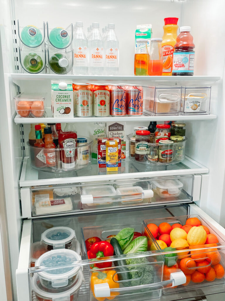 A meticulously organized refrigerator featuring a variety of beverages, condiments, dairy products, and fresh produce. Clear storage bins and containers keep items neatly arranged, making the fridge both functional and visually appealing.