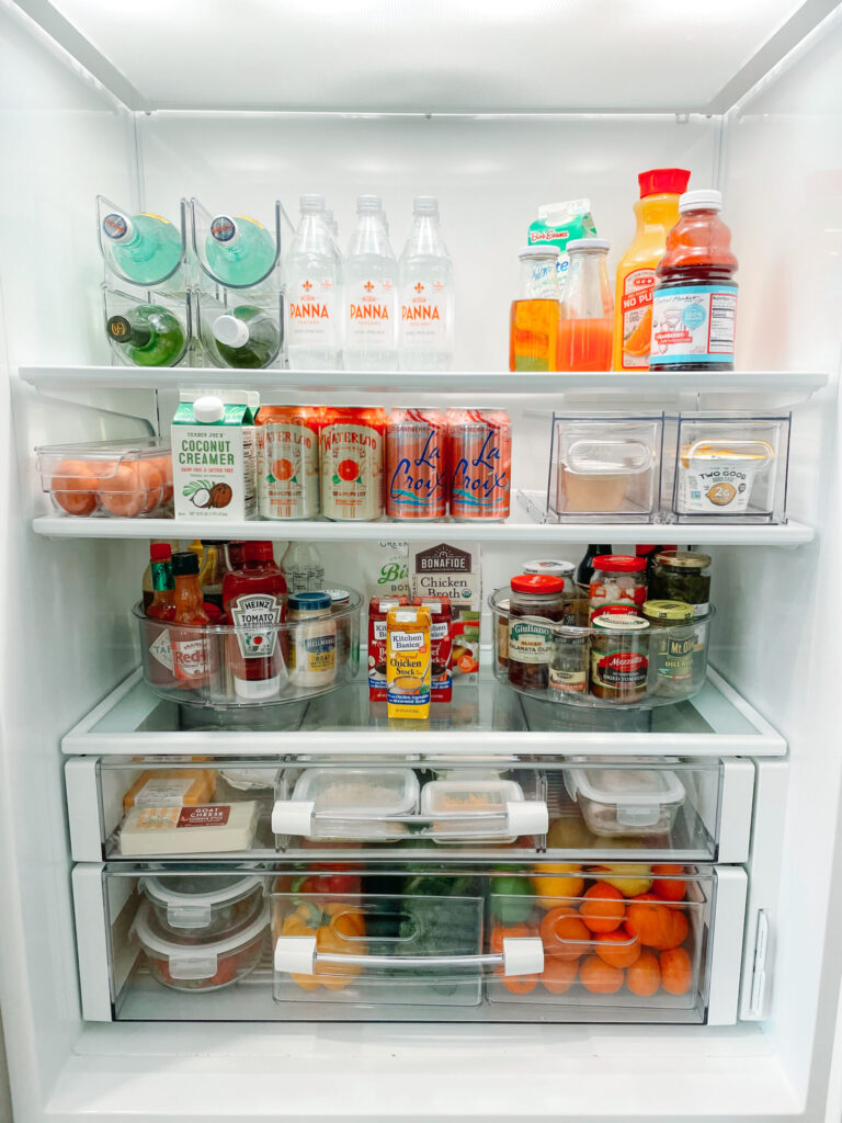 A meticulously organized refrigerator featuring a variety of beverages, condiments, dairy products, and fresh produce. Clear storage bins and containers keep items neatly arranged, making the fridge both functional and visually appealing.