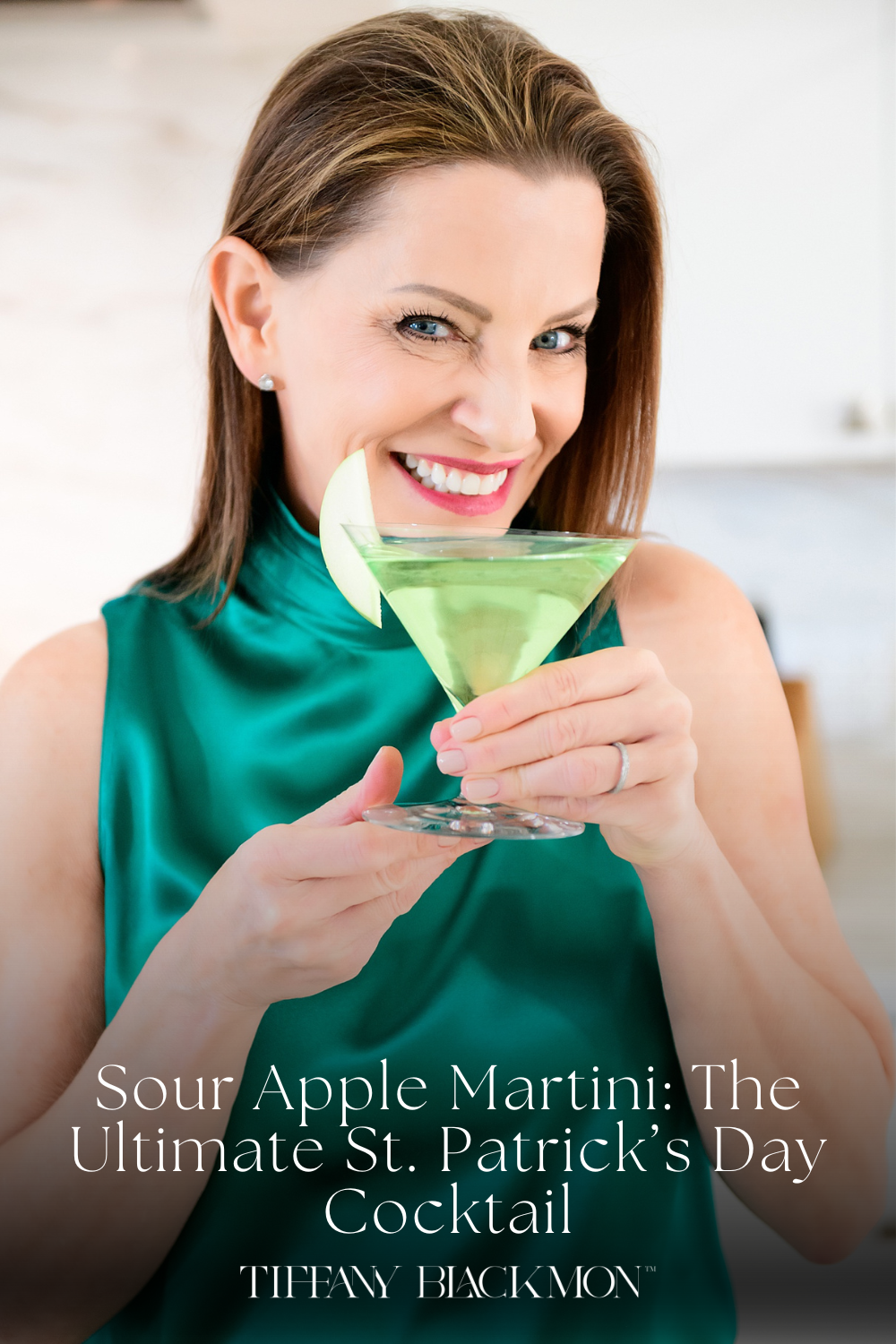 In this image, a woman is playfully peeking over a martini glass filled with a bright green cocktail. She is smiling broadly, adding a lively and engaging character to the scene. The woman is dressed in a sleek, emerald green sleeveless top, matching the drink's vibrant color. A slice of green apple is creatively placed on the rim of the glass, enhancing the visual appeal and suggesting a crisp, refreshing taste. The light, bright background keeps the focus on her and the cocktail, emphasizing a fun and elegant atmosphere.